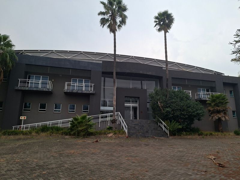 Front elevation of a large industrial building featuring a paved driveway, stone staircase, glass entrance, and multiple balconies with metal railings.