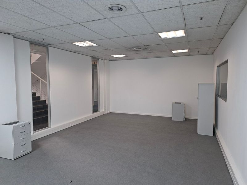 A clean, vacant office space featuring a suspended ceiling, recessed lighting, carpeted flooring, and glass partition walls, offering a professional and functional work environment.