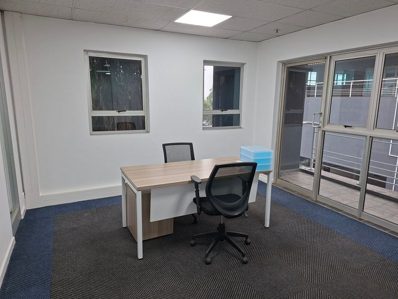 A professional office space featuring carpeted flooring, recessed ceiling lighting, and large aluminium-framed windows with access to an external balcony area.