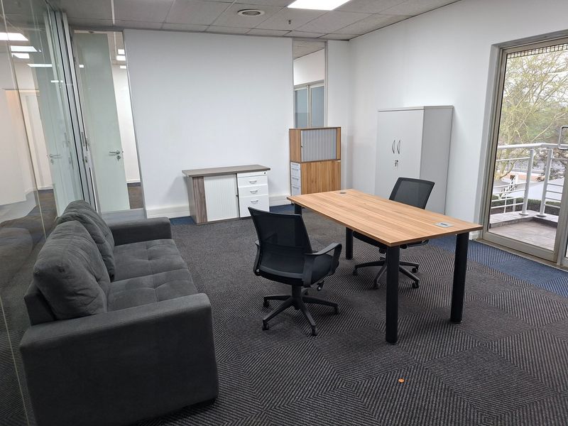 A professional office space featuring a suspended ceiling, recessed lighting, carpeted flooring, and a glass partition wall with direct access to a balcony.