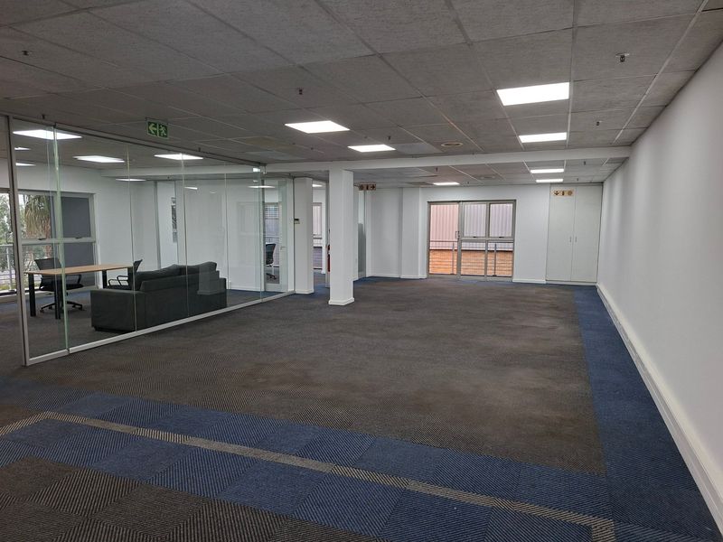 Spacious open-plan office area featuring glass partitions, suspended ceilings with recessed lighting, and built-in storage cupboards, offering a versatile workspace layout.