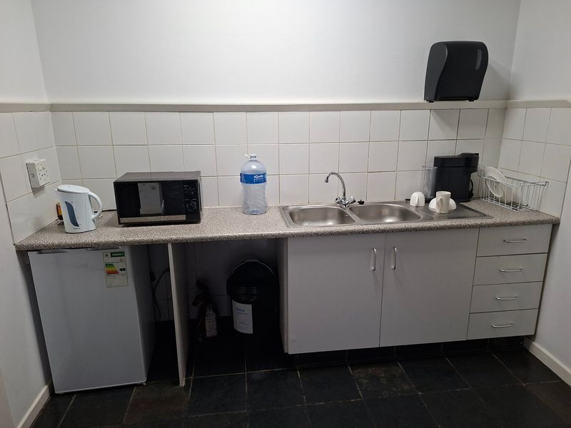 A functional industrial kitchenette featuring a double stainless steel sink, laminate countertops, tiled backsplash, and ample built-in storage cabinetry.