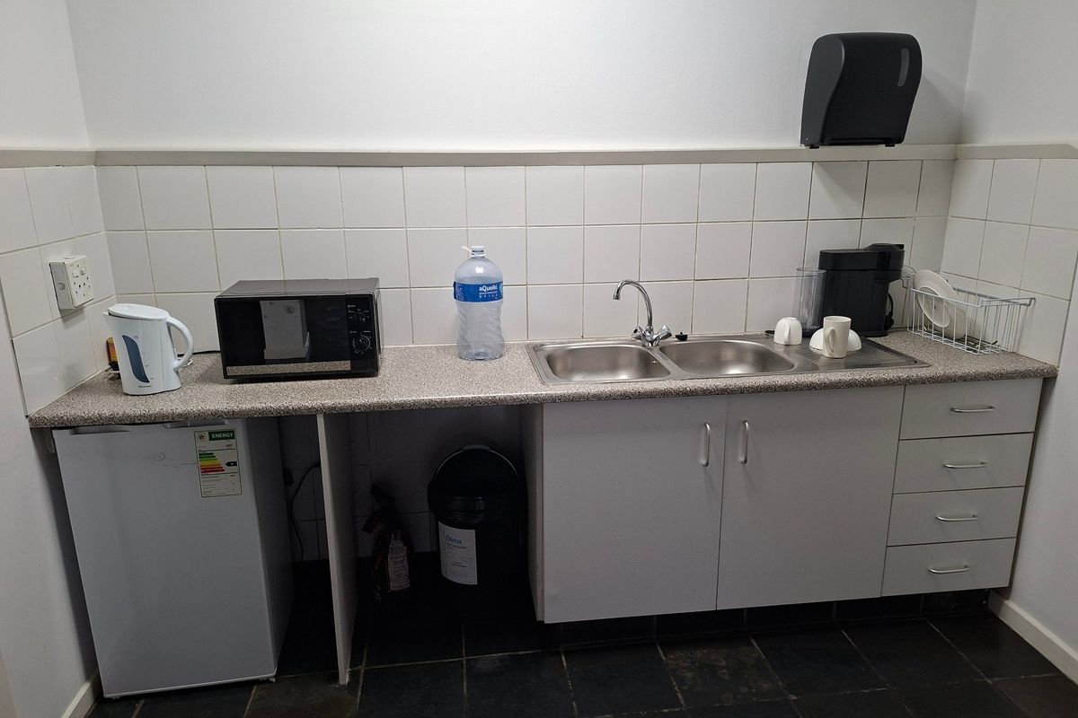 A functional industrial kitchenette featuring a double stainless steel sink, laminate countertops, tiled backsplash, and ample built-in storage cabinetry.