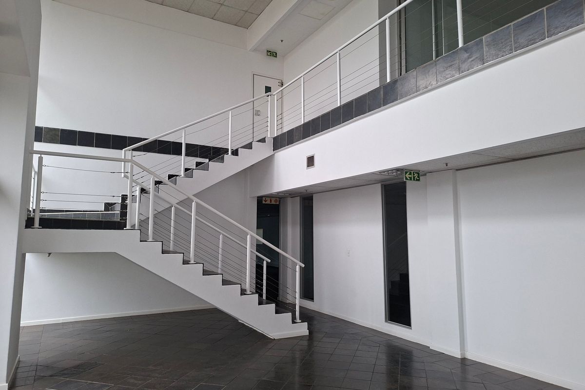 Spacious industrial entrance foyer featuring a modern staircase with metal balustrades, tiled flooring, and high ceilings.