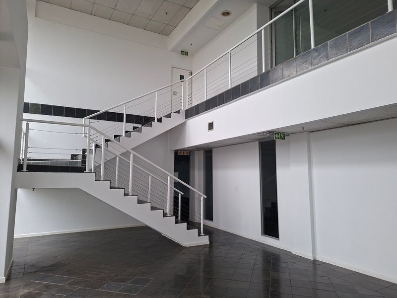 Spacious industrial entrance foyer featuring a modern staircase with metal balustrades, tiled flooring, and high ceilings.