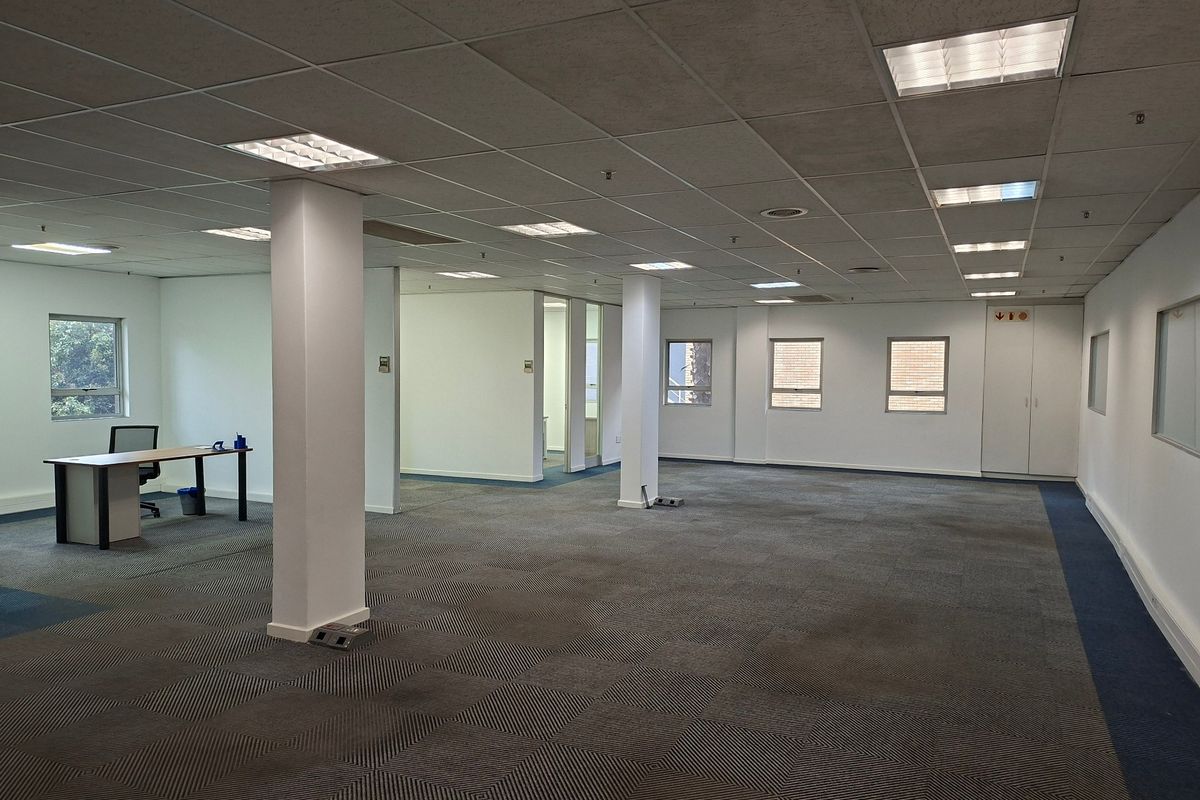 Spacious open-plan office area featuring suspended ceilings, recessed lighting, carpeted flooring, and integrated storage cupboards, offering a versatile workspace layout.