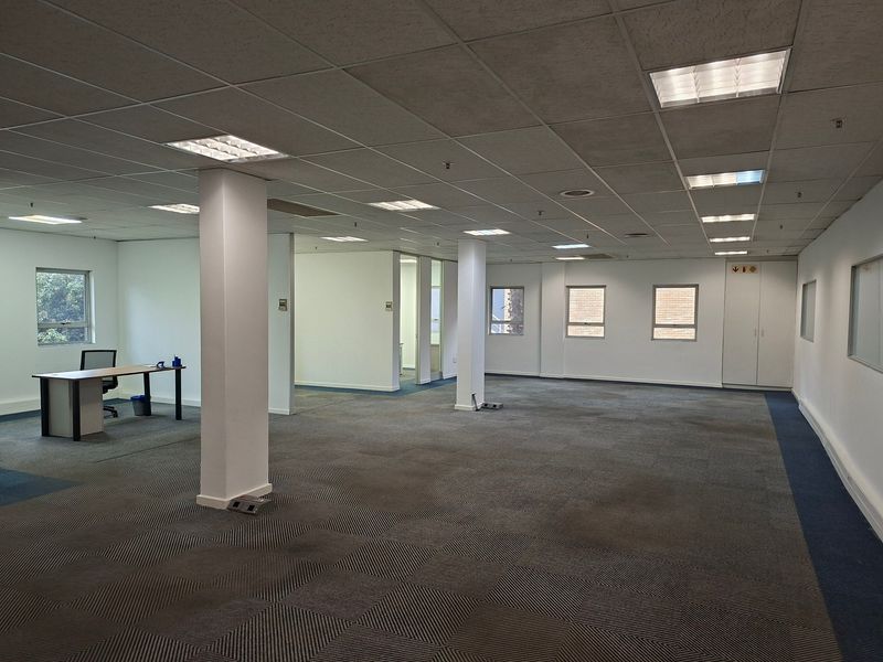 Spacious open-plan office area featuring suspended ceilings, recessed lighting, carpeted flooring, and integrated storage cupboards, offering a versatile workspace layout.