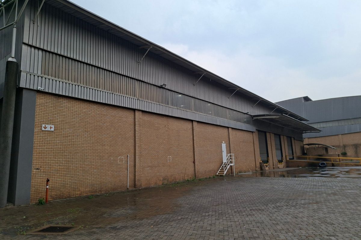 Industrial warehouse exterior featuring a face brick facade, corrugated metal cladding, and a paved loading yard area.