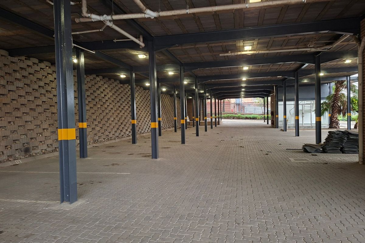 A spacious covered industrial parking area featuring steel structural columns, a paved surface, and exposed ceiling infrastructure.