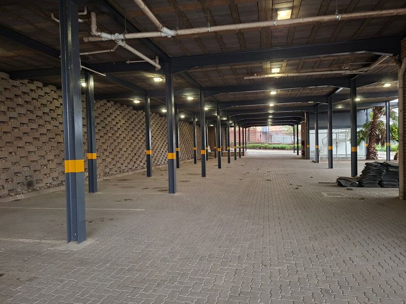A spacious covered industrial parking area featuring steel structural columns, a paved surface, and exposed ceiling infrastructure.