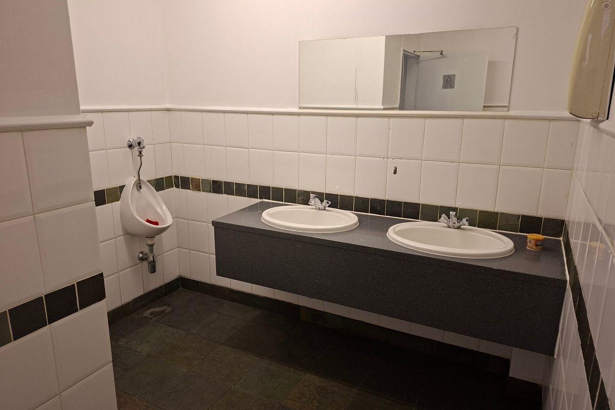 Functional industrial bathroom featuring a wall-mounted urinal, dual vanity sinks with a stone countertop, and tiled wall finishes.