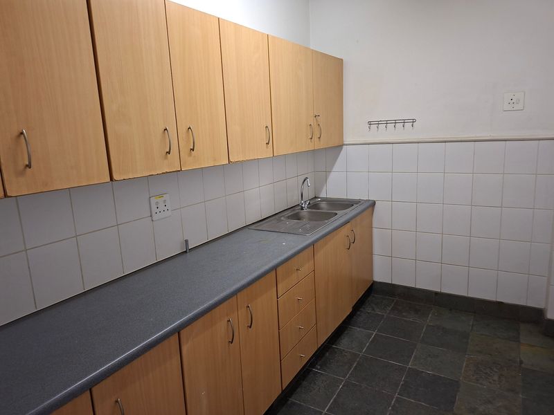 A functional scullery area featuring laminate cabinetry, a stainless steel sink, tiled splashback, and durable stone tile flooring.