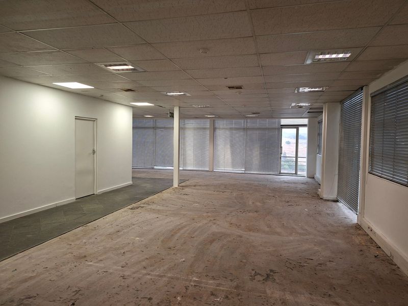 Open-plan office space featuring a suspended ceiling, recessed lighting, and large windows with venetian blinds, currently awaiting new flooring and interior finishes.