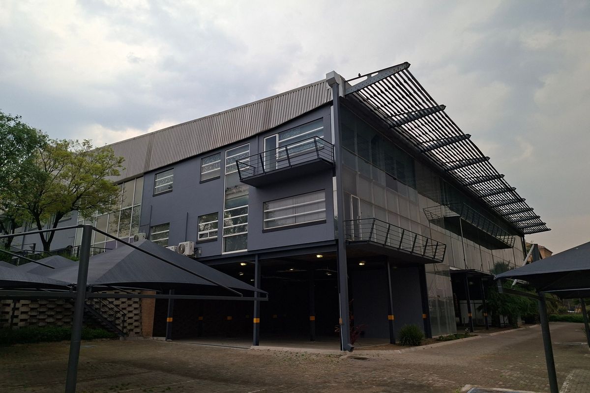Modern industrial building featuring a steel structure, metal roofing, integrated balconies, and covered parking bays with shade cloth.