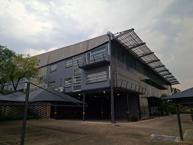 Modern industrial building featuring a steel structure, metal roofing, integrated balconies, and covered parking bays with shade cloth.