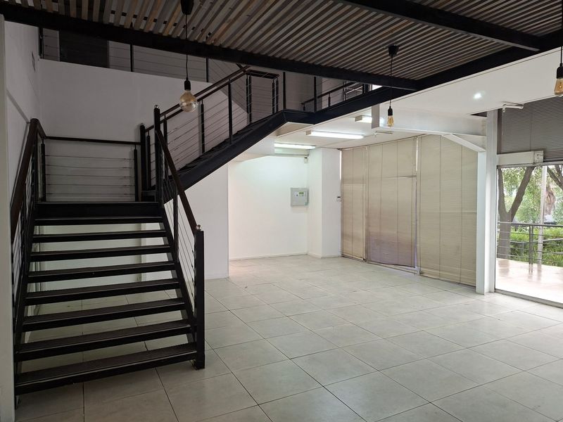 Spacious open-plan industrial area featuring a modern metal staircase, tiled flooring, exposed ceiling, and large glass doors with integrated blinds.