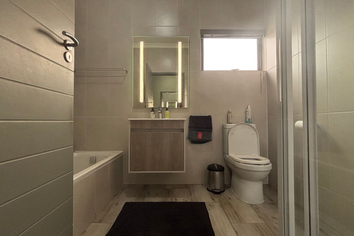 Modern bathroom featuring a built-in vanity with an illuminated mirror, a bathtub, a separate shower enclosure, and neutral wall and floor tiling.