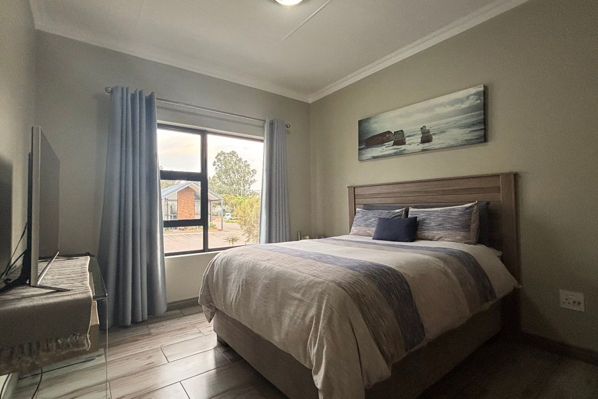 A well-maintained bedroom featuring tiled flooring, neutral wall tones, and an aluminium-framed window providing natural light.