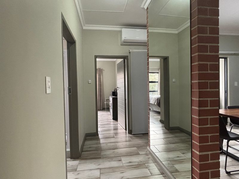 A well-lit hallway featuring tiled flooring, an exposed brick pillar, a large wall mirror, and an integrated air conditioning unit.