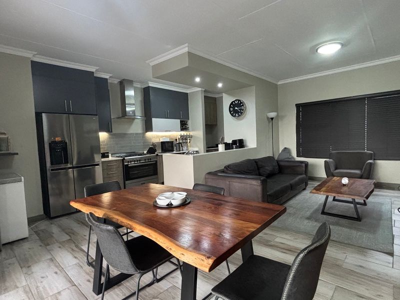 A modern open-plan living and kitchen area featuring contemporary cabinetry, stainless steel appliances, tiled flooring, and neutral wall finishes.