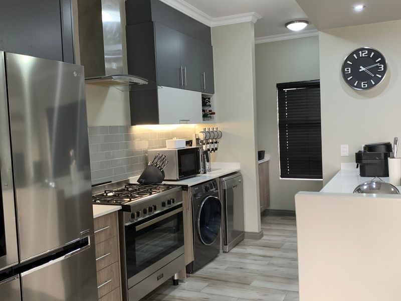 Modern kitchen featuring sleek grey and wood-tone cabinetry, stone countertops, subway tile backsplash, and integrated appliances including a gas stove and laundry unit.