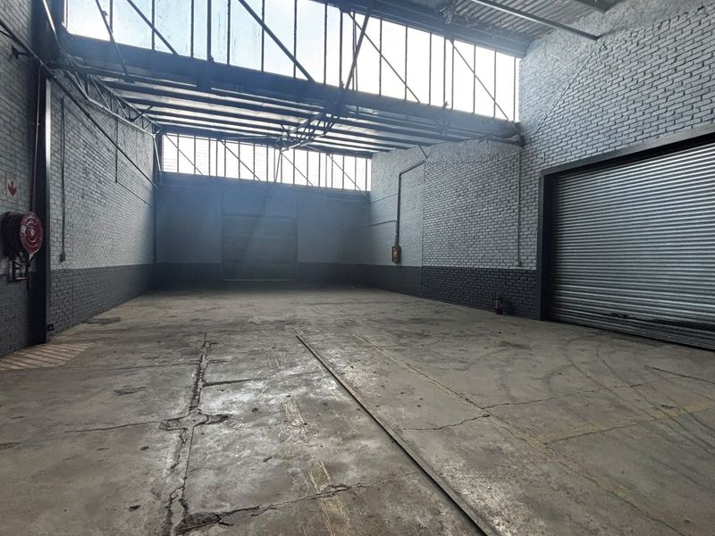 Spacious industrial warehouse unit featuring high ceilings, clerestory windows, durable concrete flooring, and a large roller shutter door for easy access.