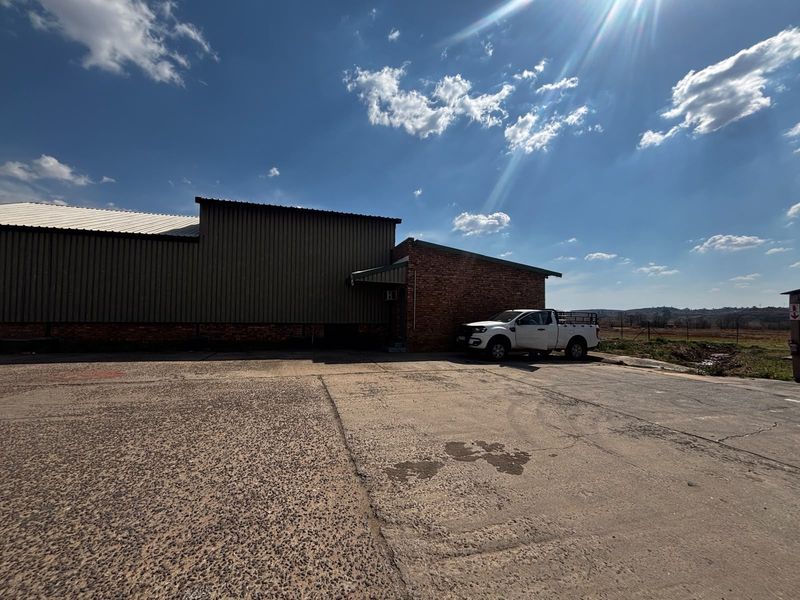 Exterior view of an industrial property featuring a combination of corrugated metal cladding and exposed brickwork with an expansive concrete yard area.