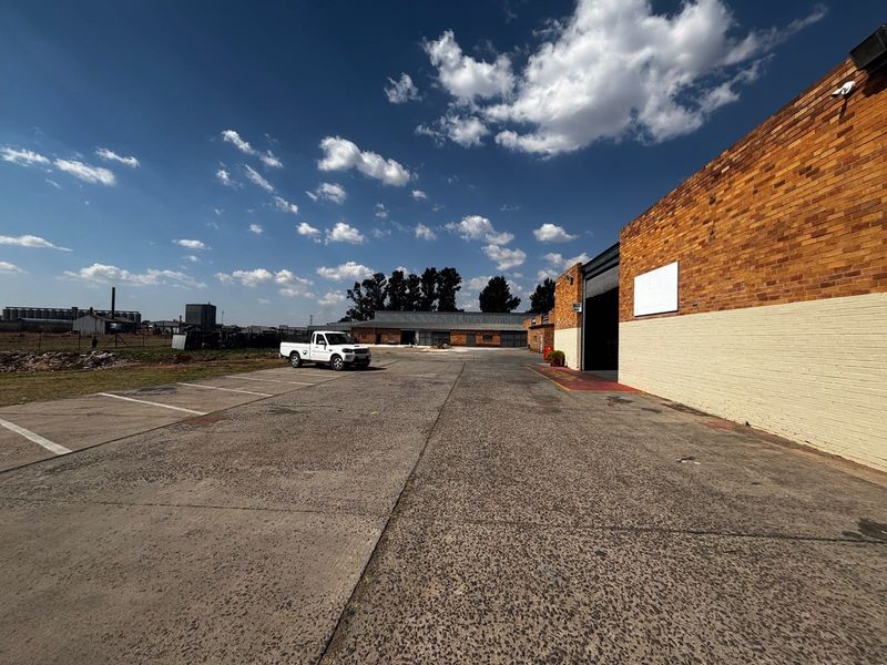 Industrial property exterior featuring a large concrete yard, brick facade, and roller shutter access, suitable for logistics or manufacturing operations.