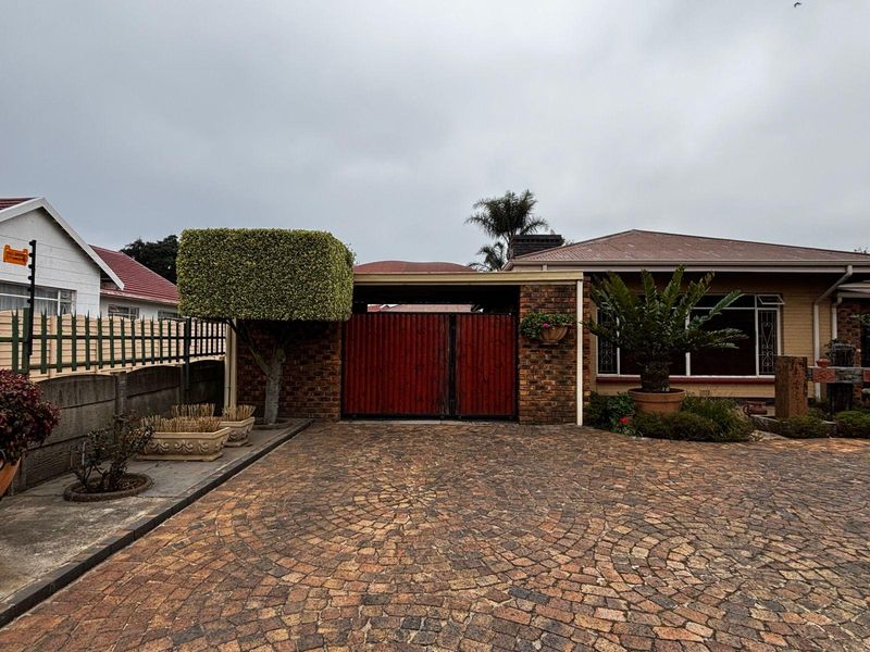 Front view of the property featuring a paved brick driveway, facebrick facade, and a secure gated entrance with an integrated carport.