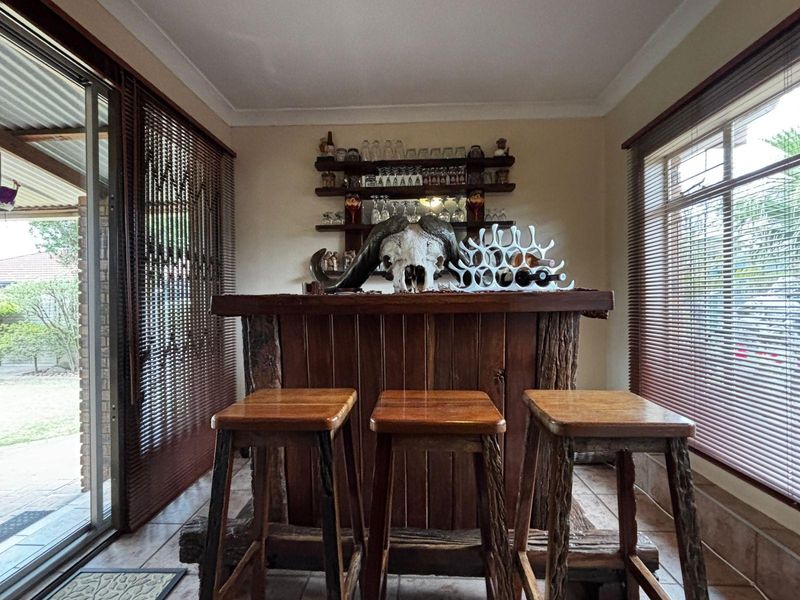 A dedicated bar area featuring a custom-built wooden counter, fixed shelving, tiled flooring, and large windows with venetian blinds providing natural light.