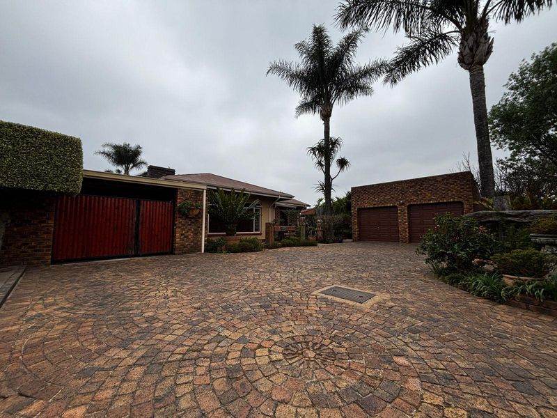 Front exterior view of the property featuring a circular pattern brick driveway, double garage, and established garden landscaping.