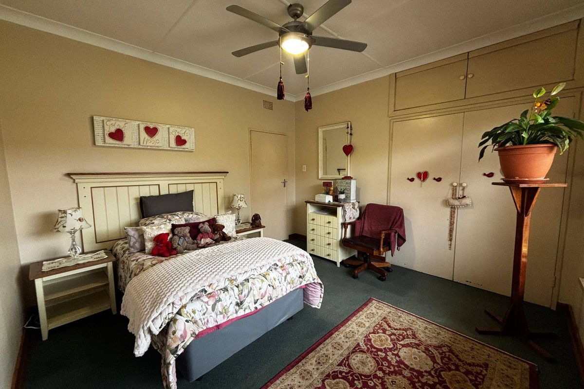 A bedroom featuring built-in cupboards, a ceiling fan, and carpeted flooring, offering a functional space with potential for modern updates.