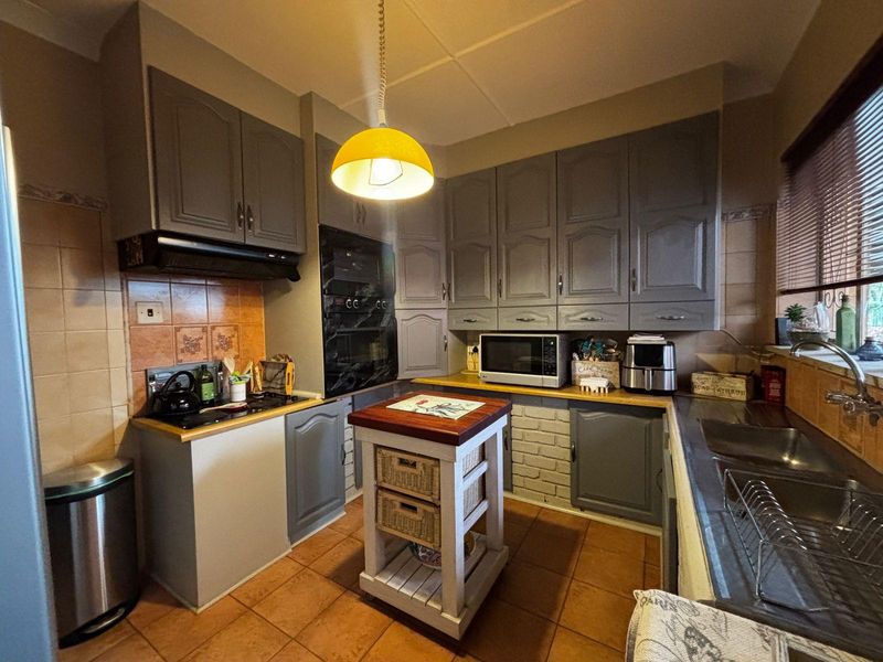 A functional kitchen featuring grey built-in cabinetry, a built-in oven, hob, extractor fan, and a double sink with tiled flooring and backsplash.