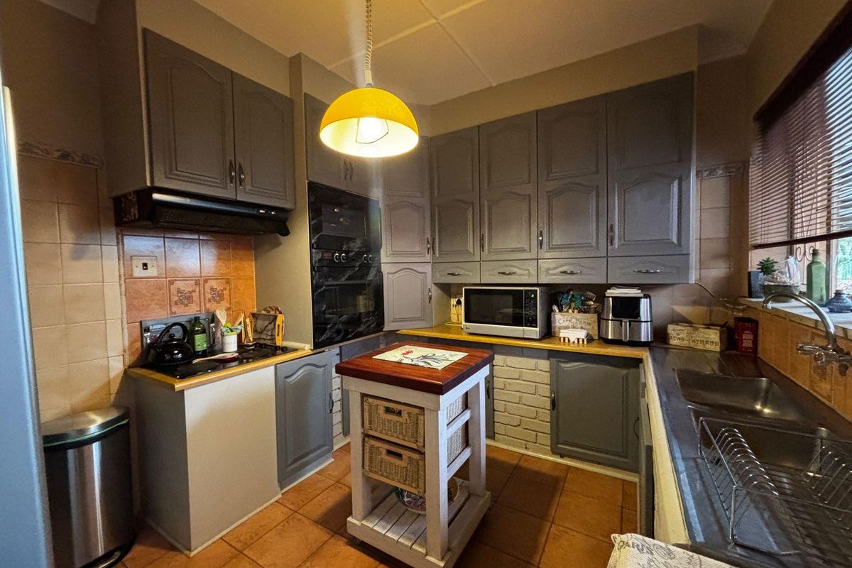 A functional kitchen featuring grey built-in cabinetry, a built-in oven, hob, extractor fan, and a double sink with tiled flooring and backsplash.