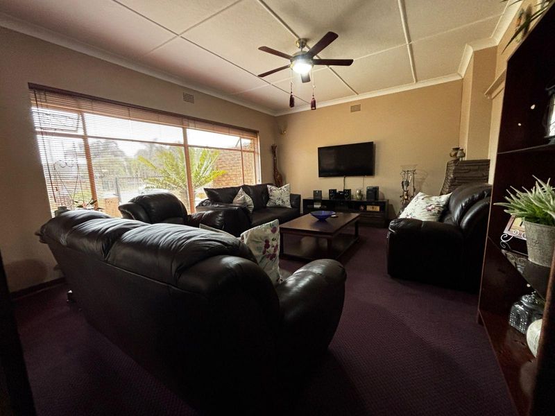 A comfortable living room featuring a large window with venetian blinds, a ceiling fan, and a wall-mounted television setup.
