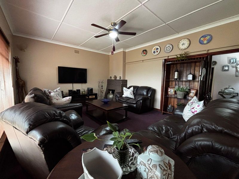 A comfortable living room featuring a brick fireplace, ceiling fan, and tiled ceiling, offering a traditional and functional space for relaxation.