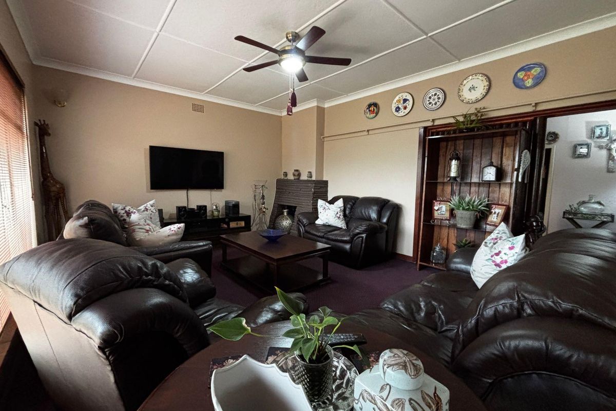 A comfortable living room featuring a brick fireplace, ceiling fan, and tiled ceiling, offering a traditional and functional space for relaxation.