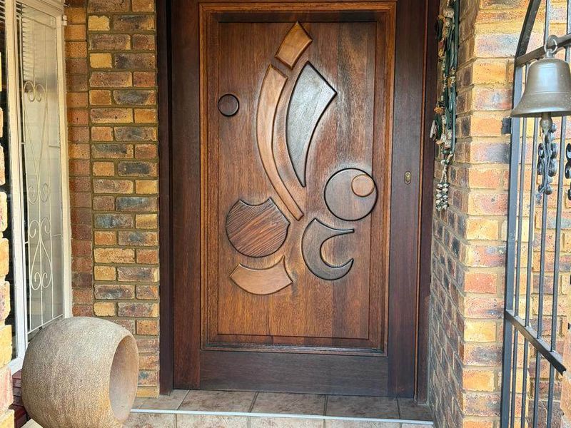 A welcoming entrance featuring a unique, custom-carved solid wood front door set within a classic face brick facade and tiled step.