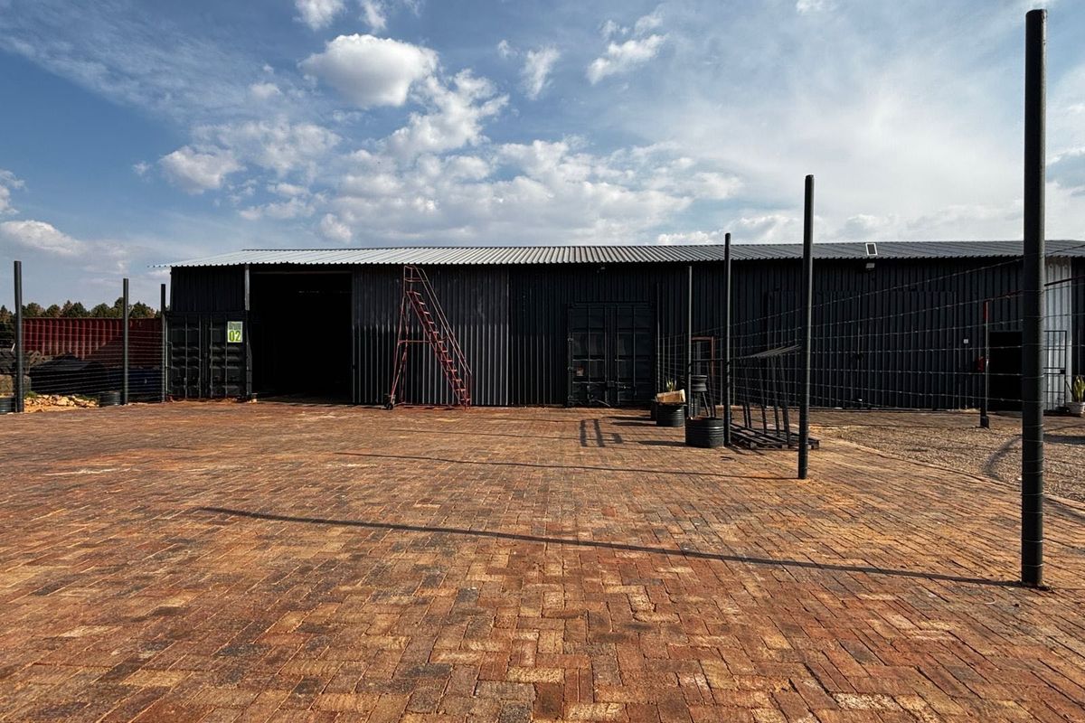 Industrial property featuring a large paved yard area and a corrugated metal warehouse structure with sliding access doors.