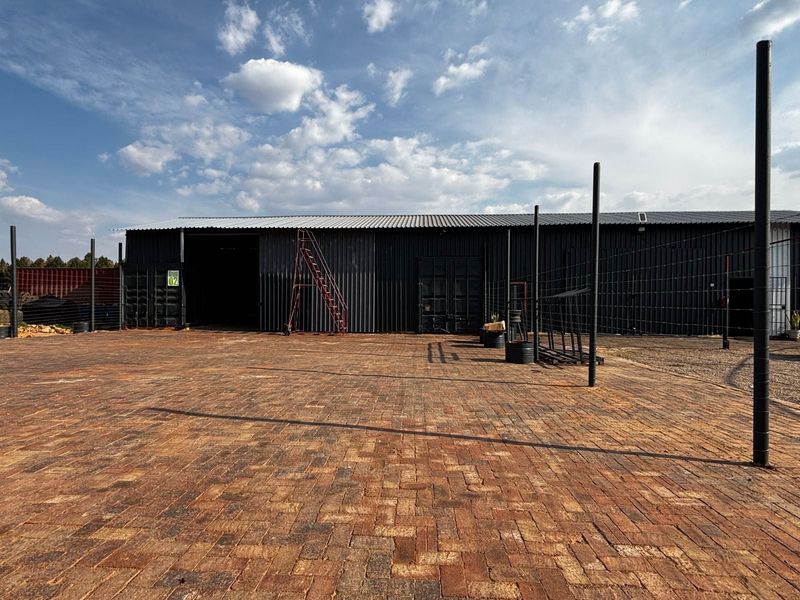 Industrial property featuring a large paved yard area and a corrugated metal warehouse structure with sliding access doors.