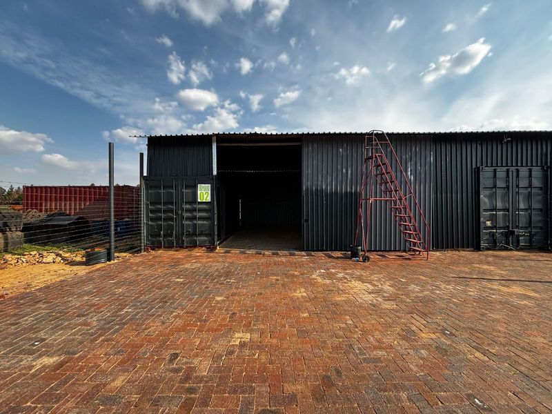 Industrial warehouse facility featuring corrugated metal cladding, a large sliding entrance, and a spacious paved forecourt area.