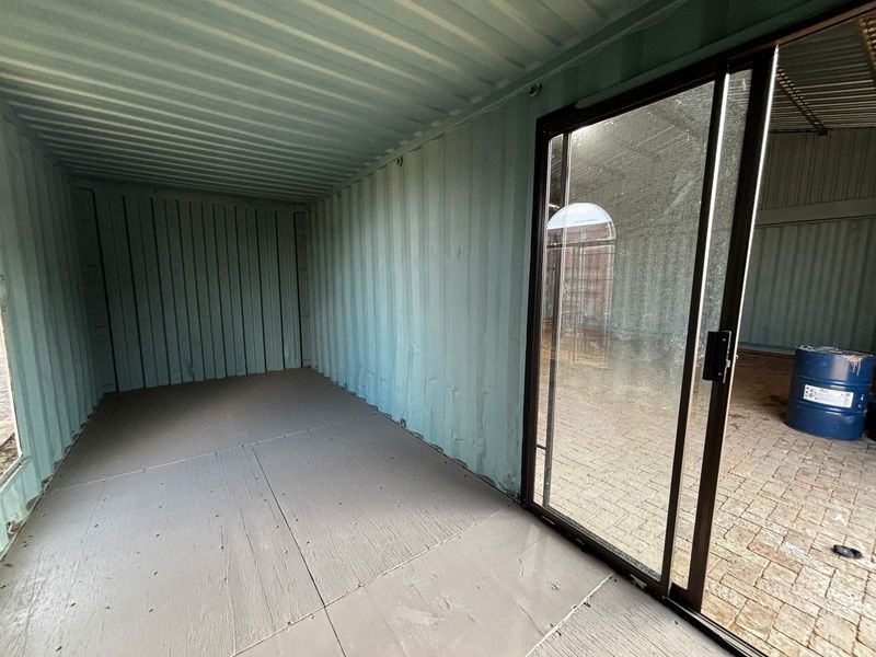 An empty utility space constructed from a converted shipping container, featuring corrugated metal walls and a sliding glass door entrance.
