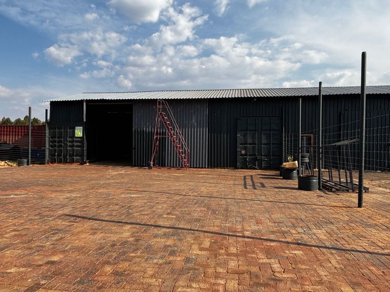 Industrial warehouse exterior featuring corrugated metal cladding, large sliding access doors, and a spacious paved yard area with security fencing.