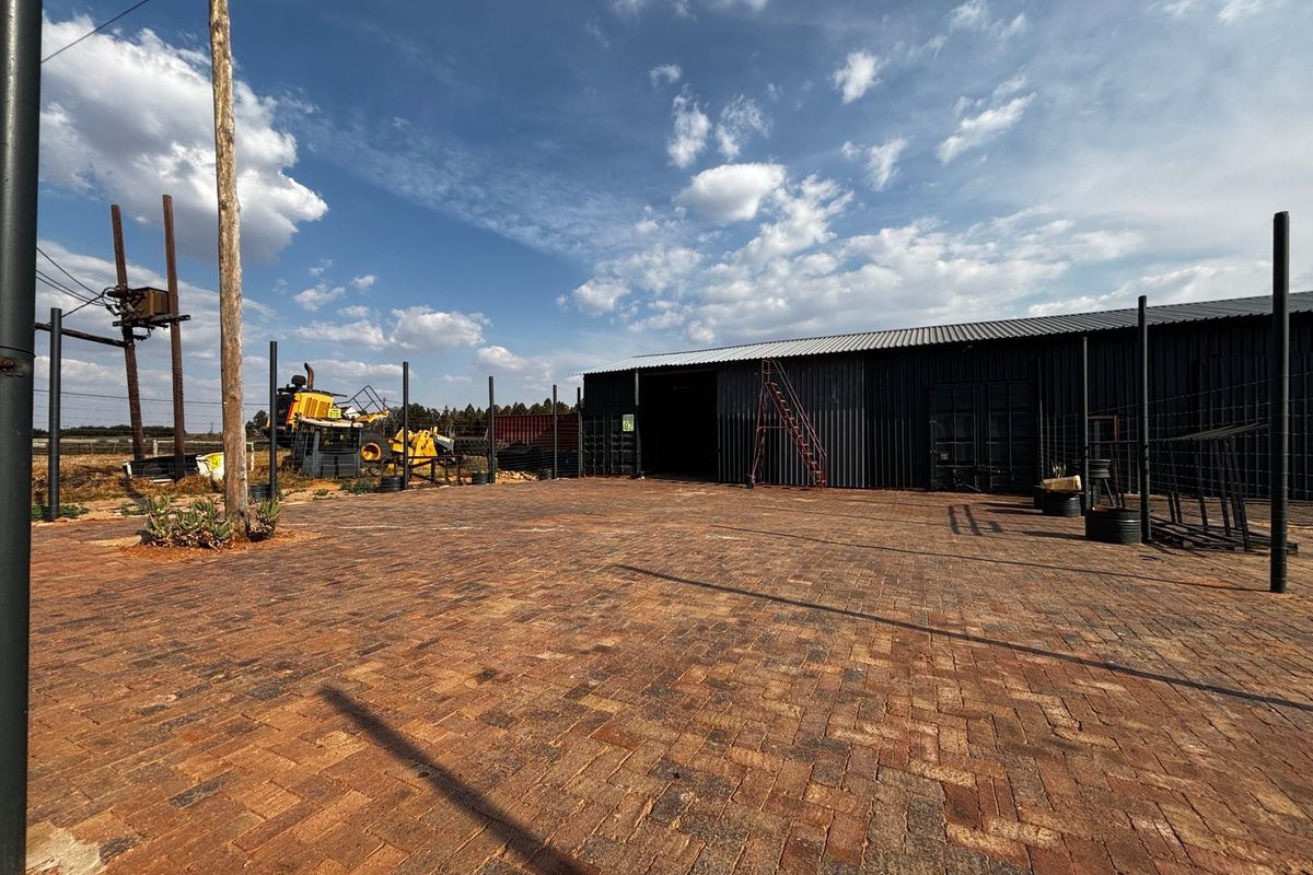 Spacious industrial property featuring a large paved yard and a corrugated metal warehouse structure.