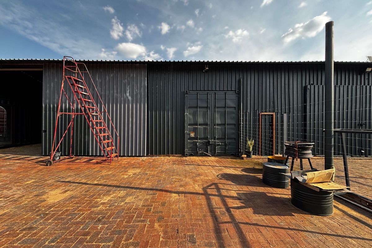 Rear industrial exterior featuring corrugated metal cladding, shipping container style doors, and a large brick-paved courtyard area.