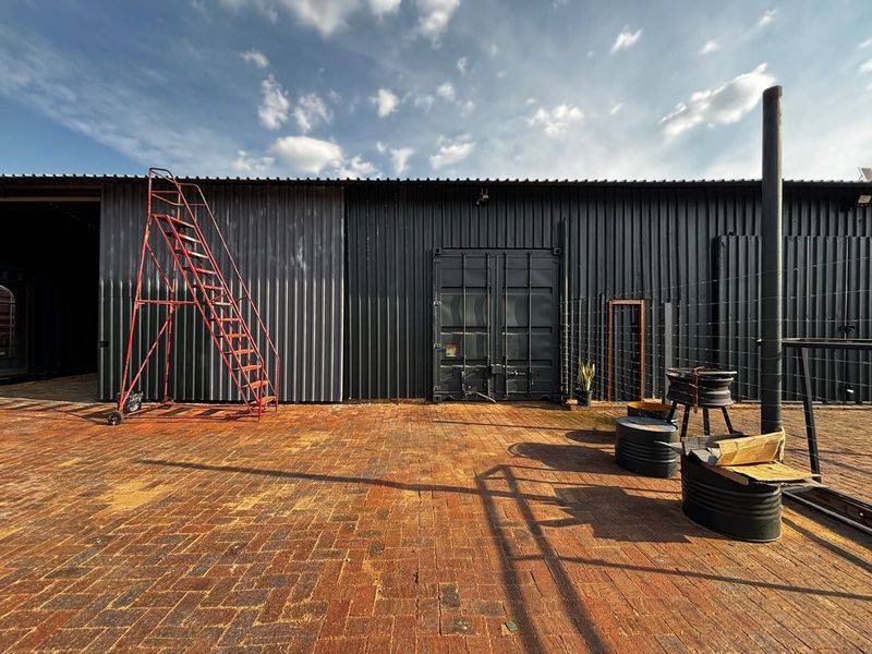 Rear industrial exterior featuring corrugated metal cladding, shipping container style doors, and a large brick-paved courtyard area.