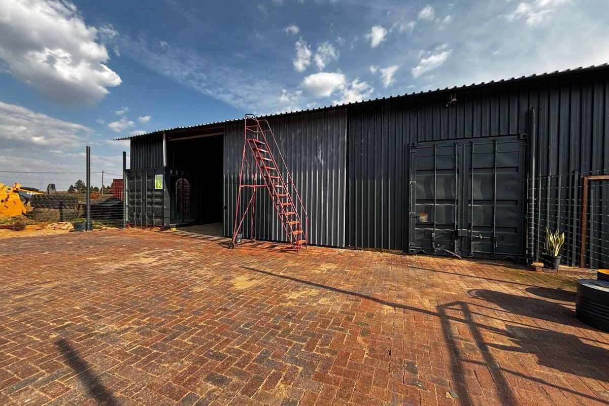Industrial warehouse facility featuring corrugated metal cladding, shipping container construction, and a spacious paved exterior yard area.
