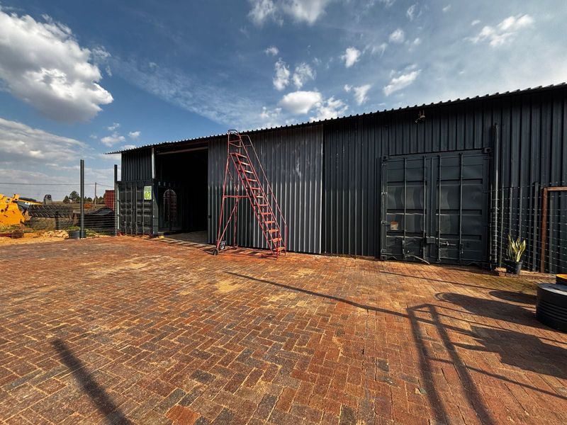Industrial warehouse facility featuring corrugated metal cladding, shipping container construction, and a spacious paved exterior yard area.