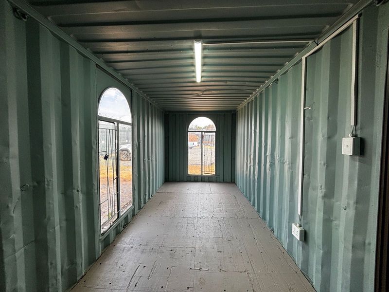 An empty industrial container space featuring corrugated steel walls, arched windows, fluorescent lighting, and basic electrical installations, suitable for various utility or storage purposes.