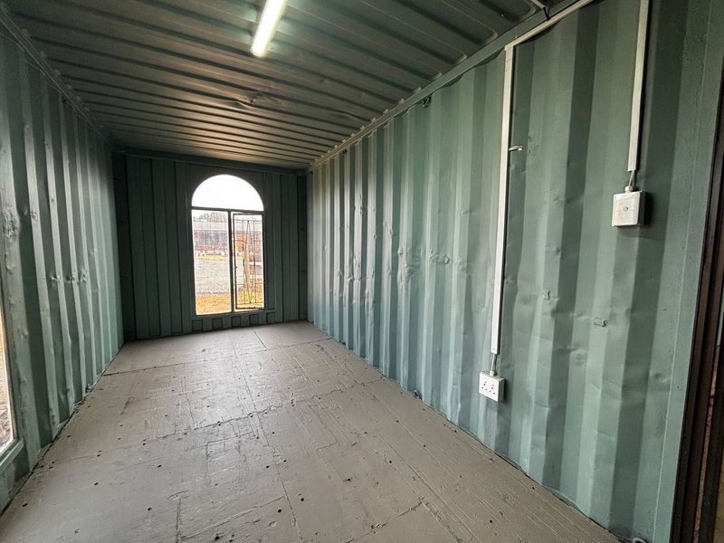An empty industrial-style utility space featuring corrugated steel walls, an arched window, and surface-mounted electrical fixtures.